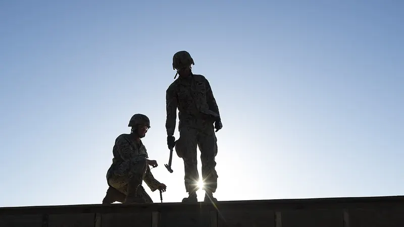 Silhouettes of two workers standing on a roof against the sky
