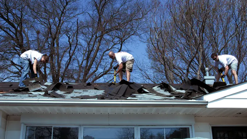 Workers stripping old shingles from a roof